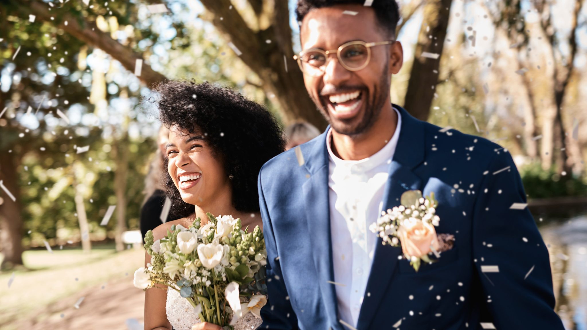 Newlywed young couple getting showered with confetti outdoors on their wedding day